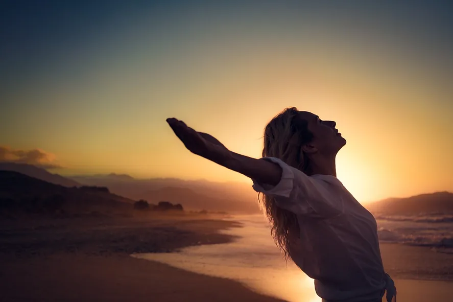 mujer con manos extendidas al atardecer